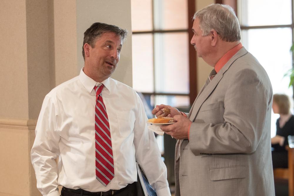 Two men, one holding a plate of food, talk at the reception